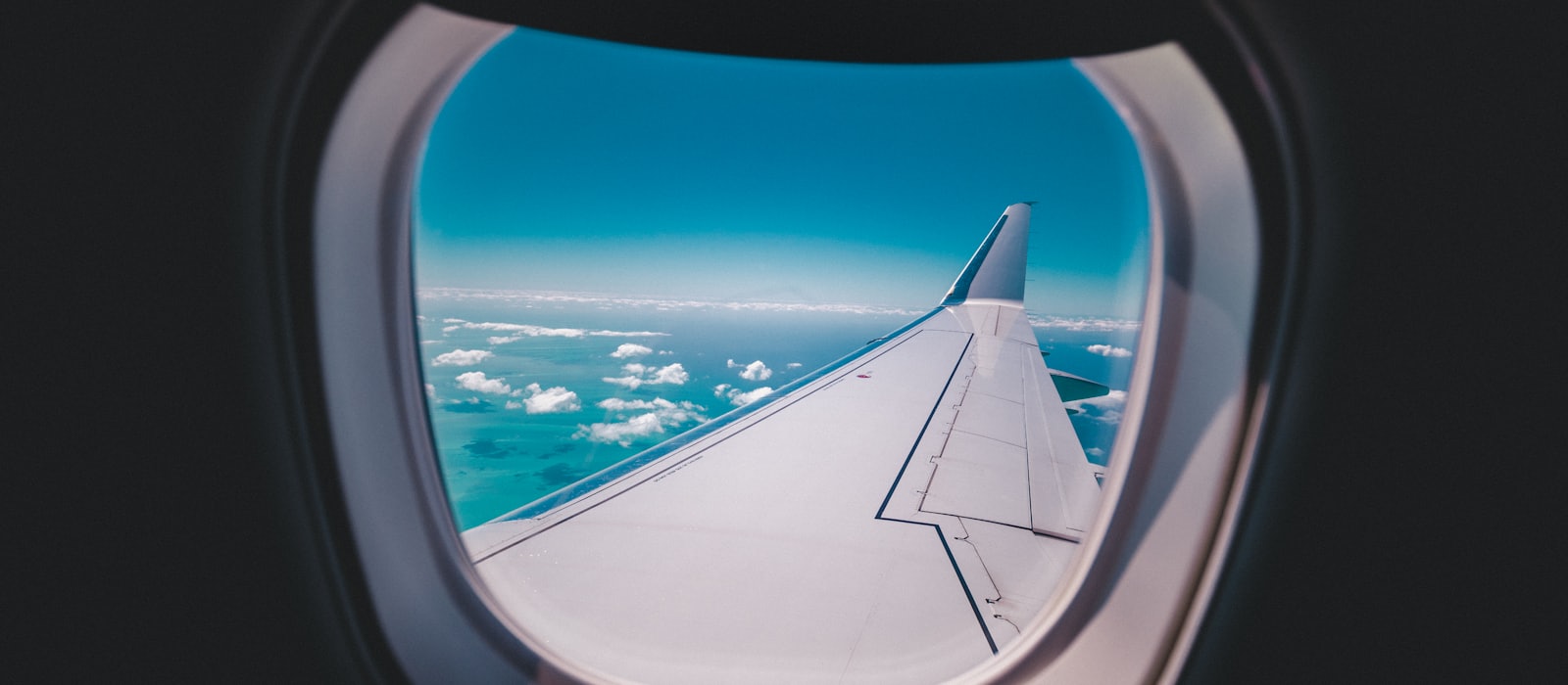 An aircraft wing seen through a cabin window above the clouds