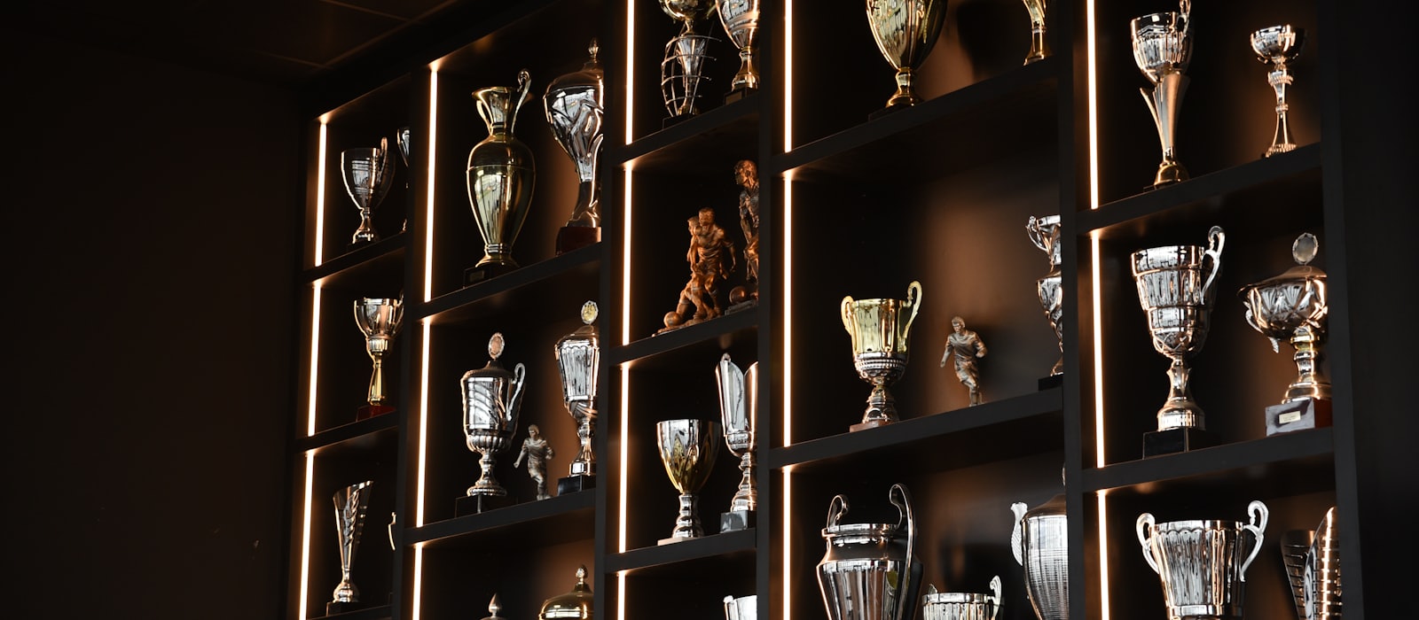 Shelves of silver and gold trophies lit from behind in a dark room
