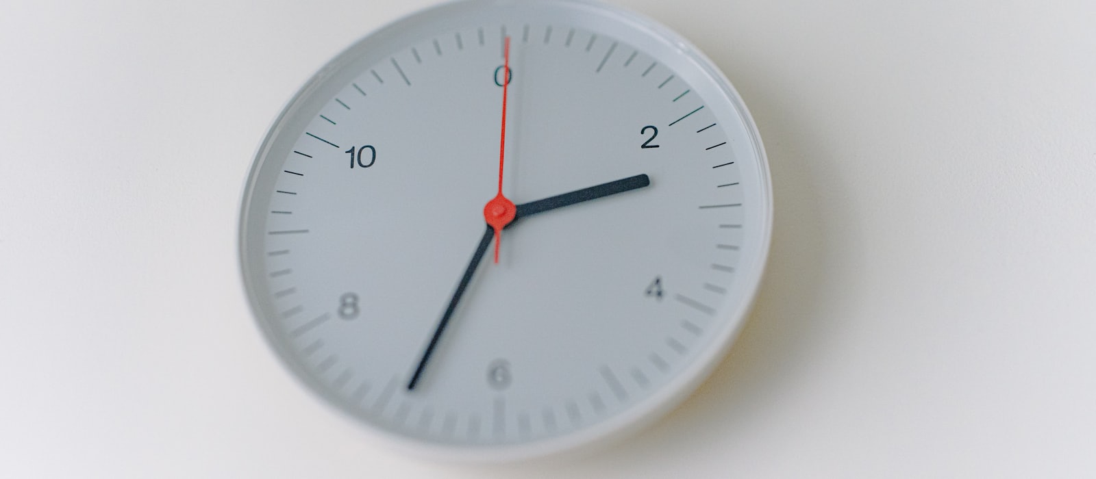 A plain white wall clock with a red second hand