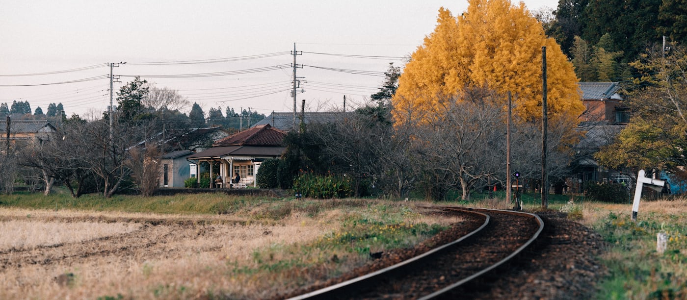 A single railway track curving past a rural station in autumn