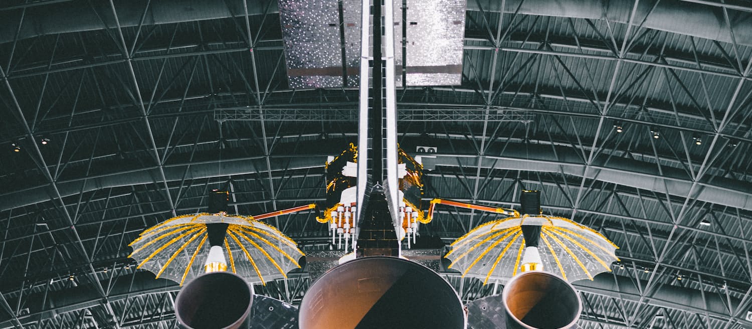 The rear of a space shuttle orbiter, engine nozzles below a hangar roof