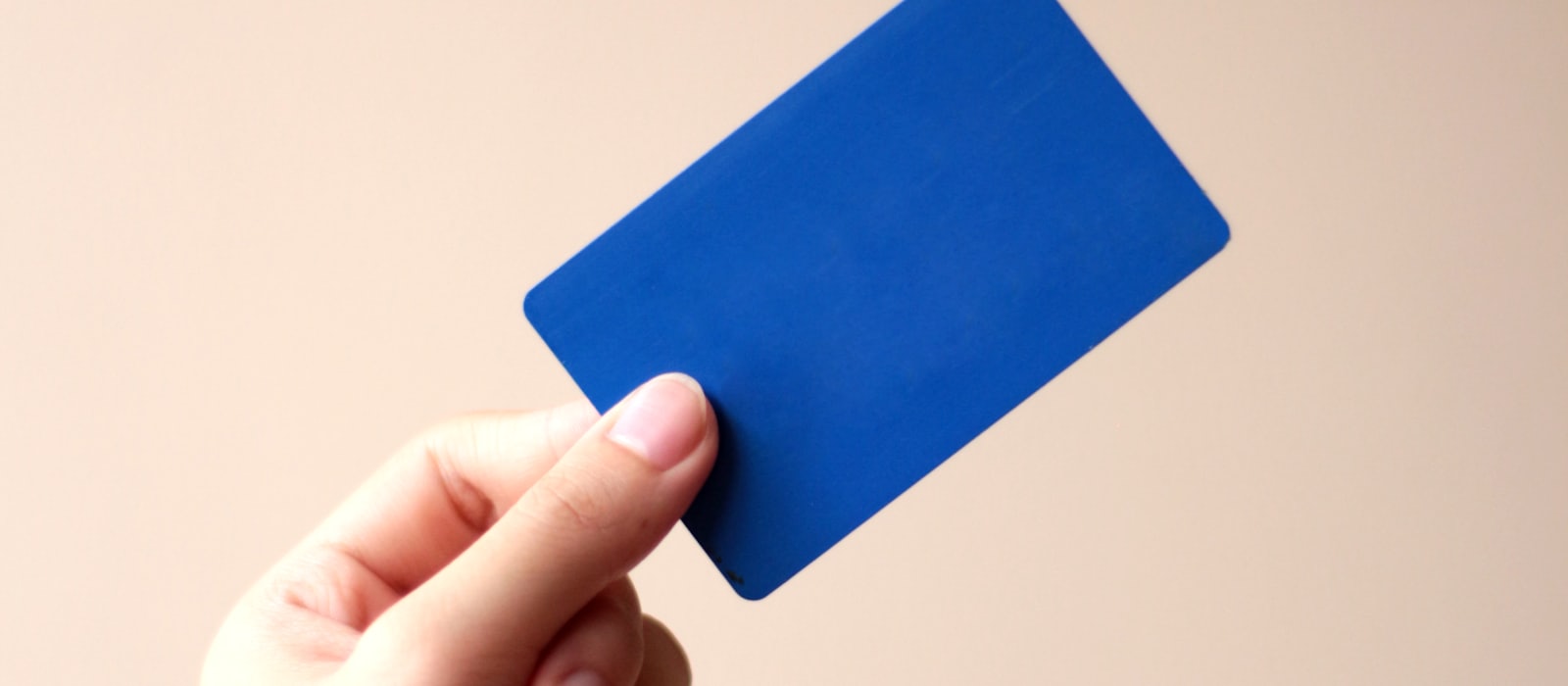 A hand holding a plain blue plastic card against a pale background