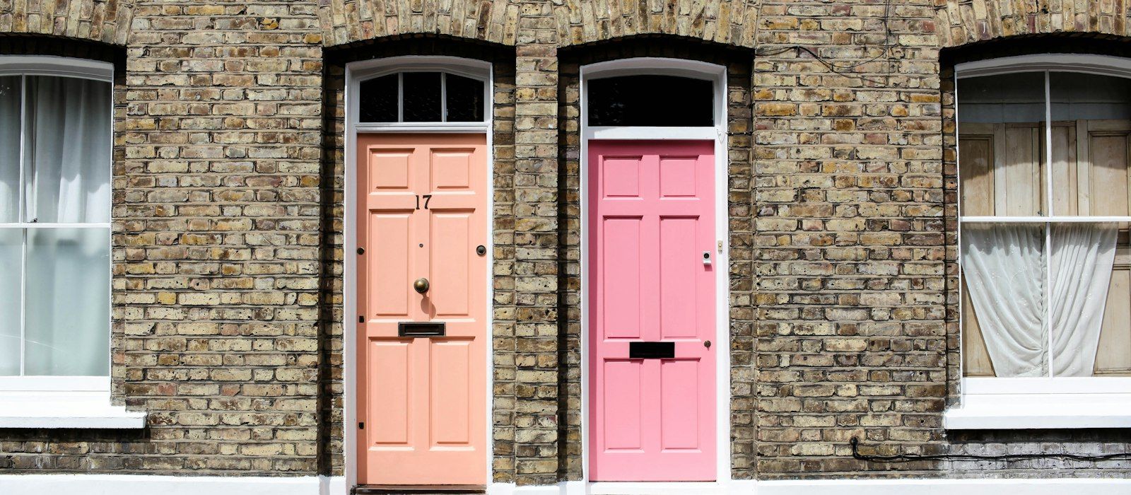 Two front doors, one peach and one pink, side by side in a brick terrace