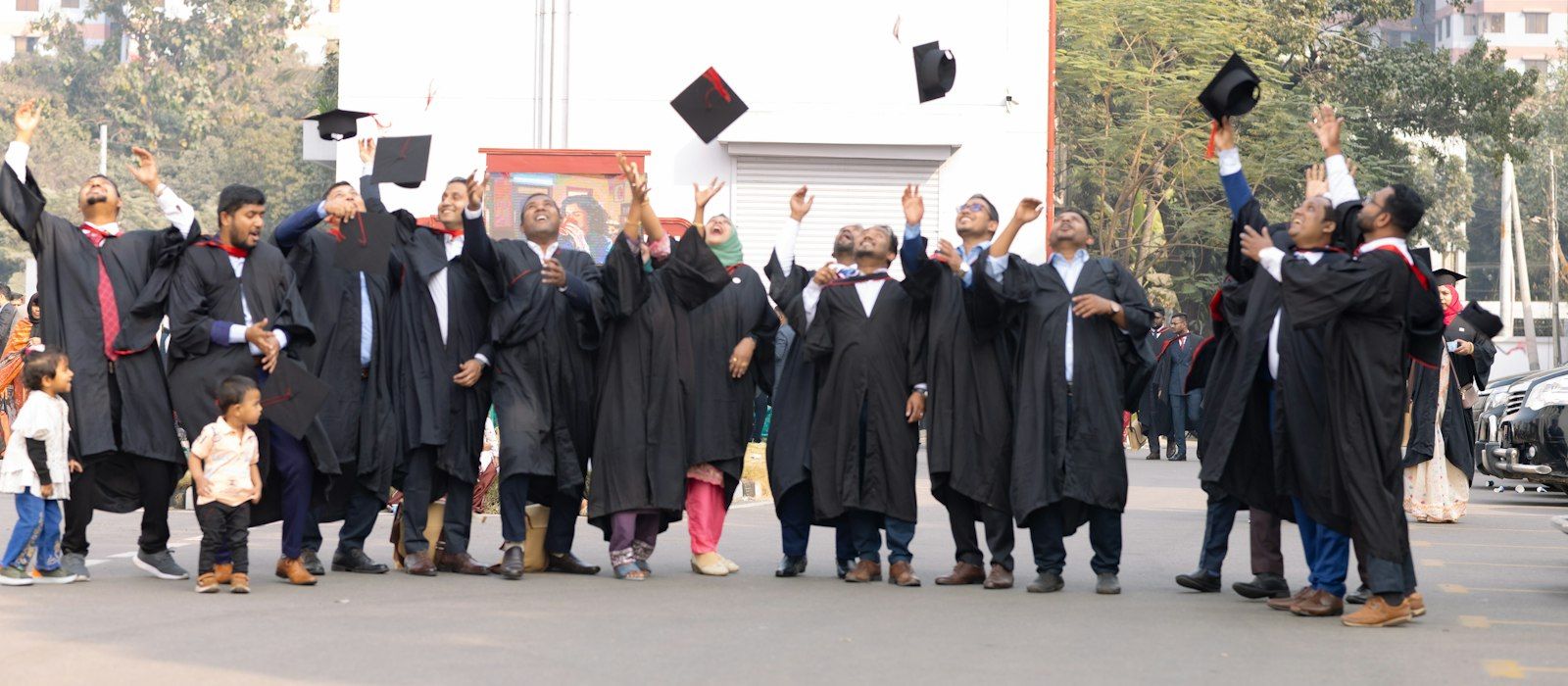 Graduates in black gowns throwing their caps in the air outdoors