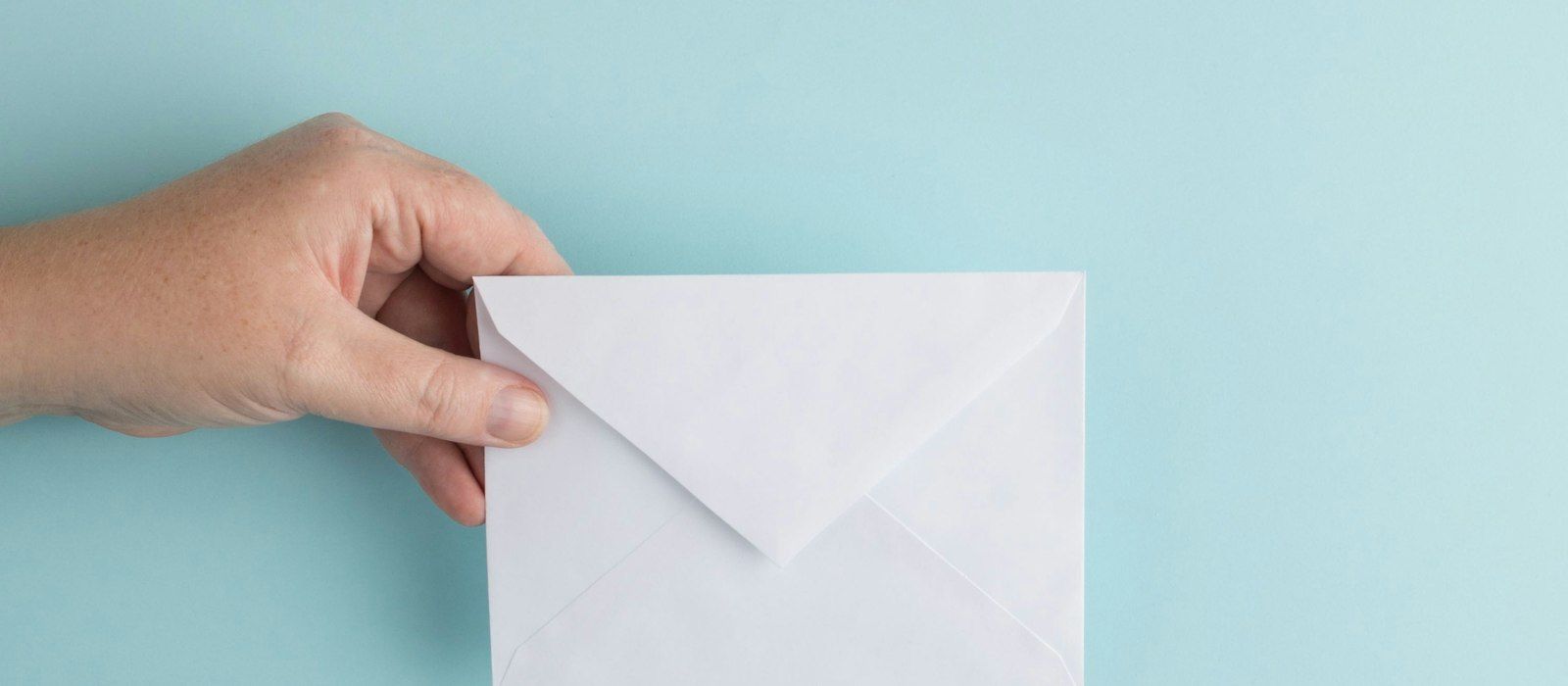 A hand holding a plain white envelope against a pale blue background