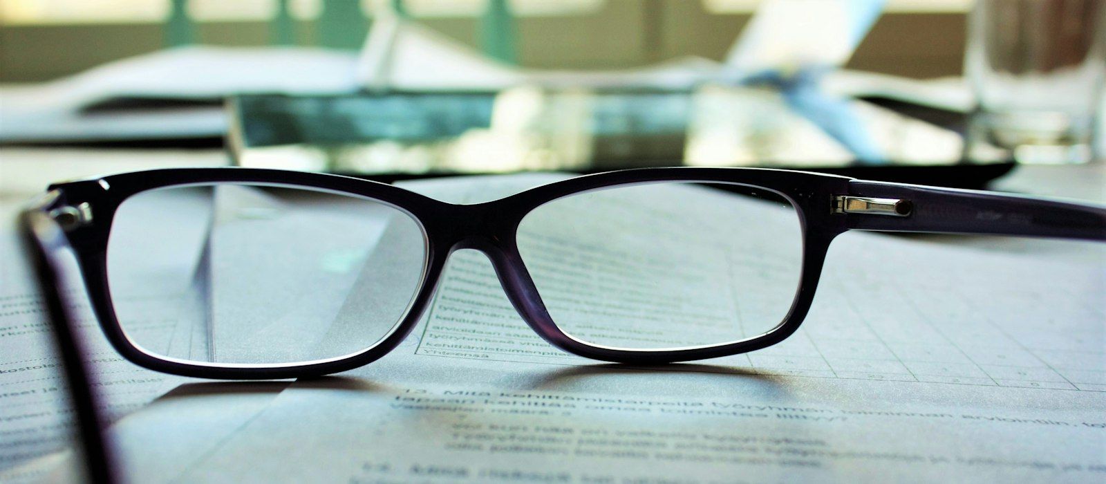 A pair of reading glasses resting on printed documents on a desk