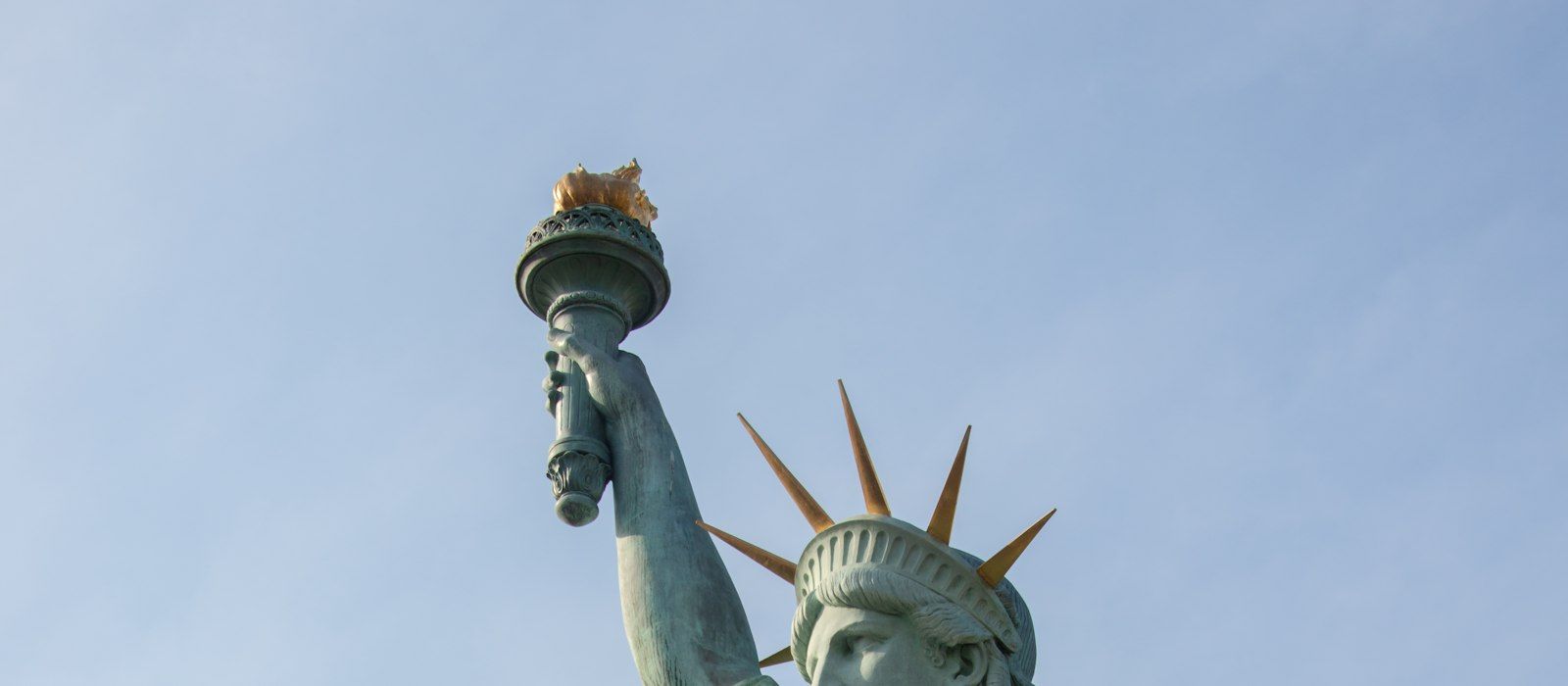 The torch and crown of the Statue of Liberty against a clear blue sky
