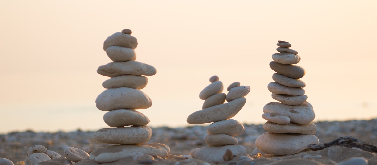 Three stacked stone cairns standing on a pebble beach at dusk