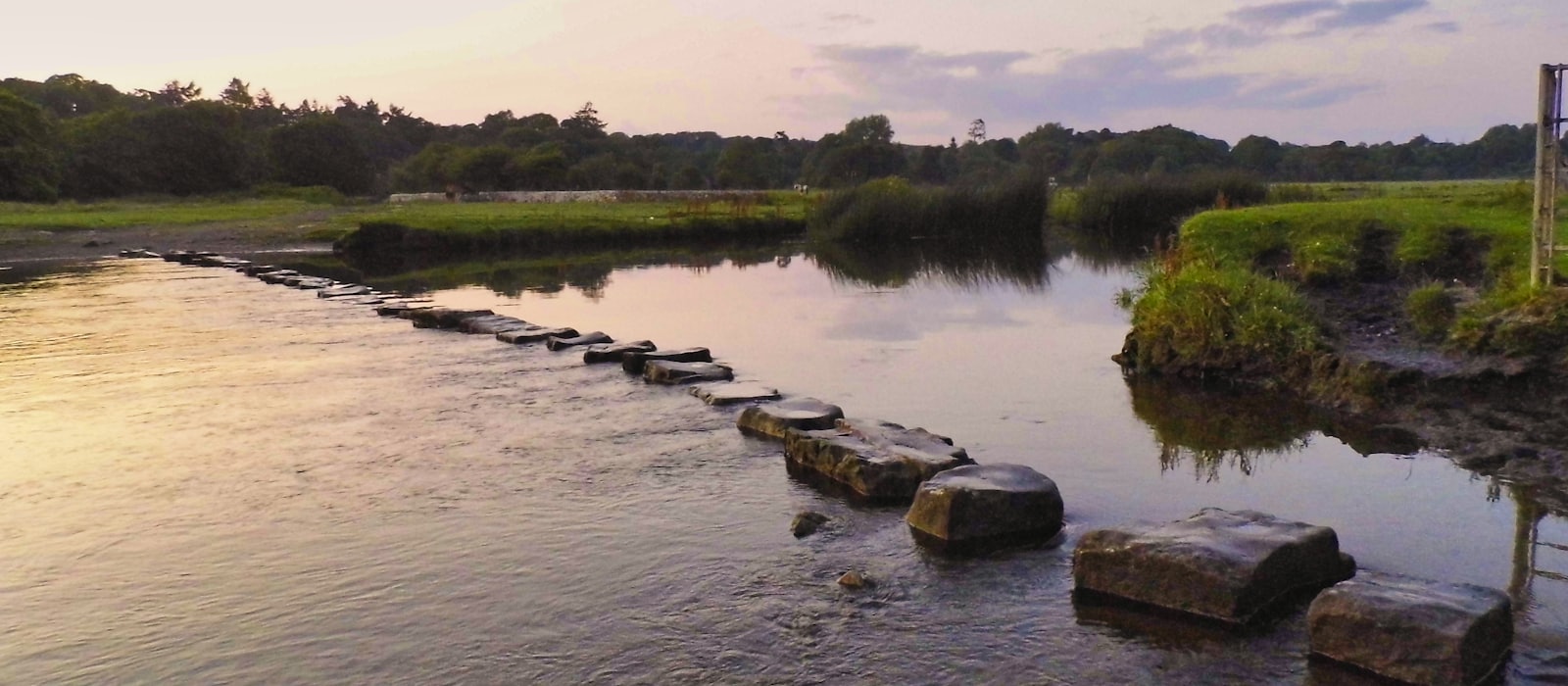 A line of stepping stones crossing a wide river at dusk