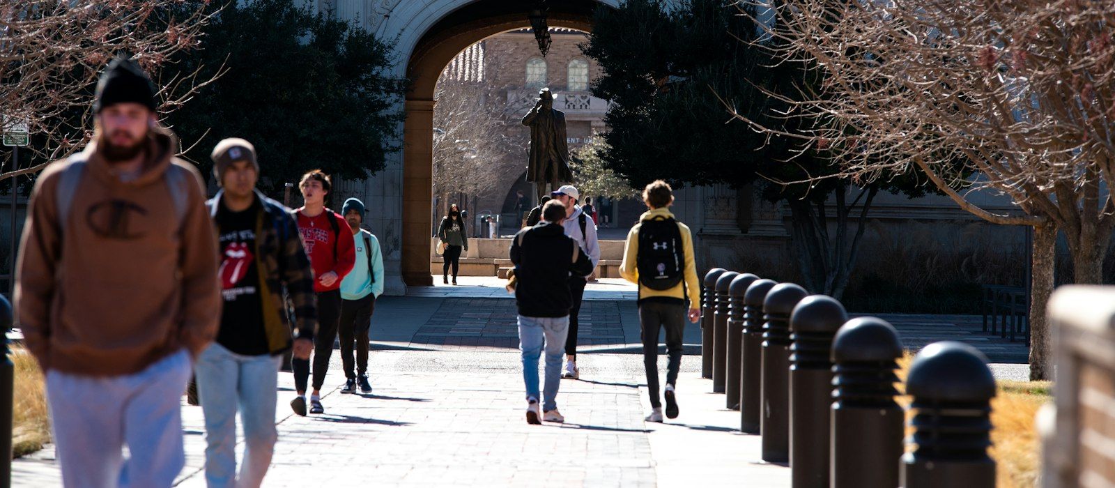 Students walking along a campus path toward a stone archway