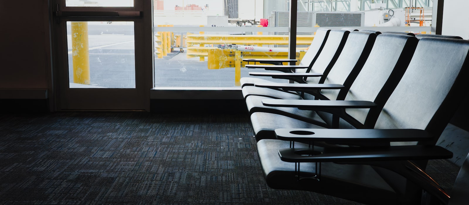 An empty row of seats at an airport departure gate, with the apron beyond the window