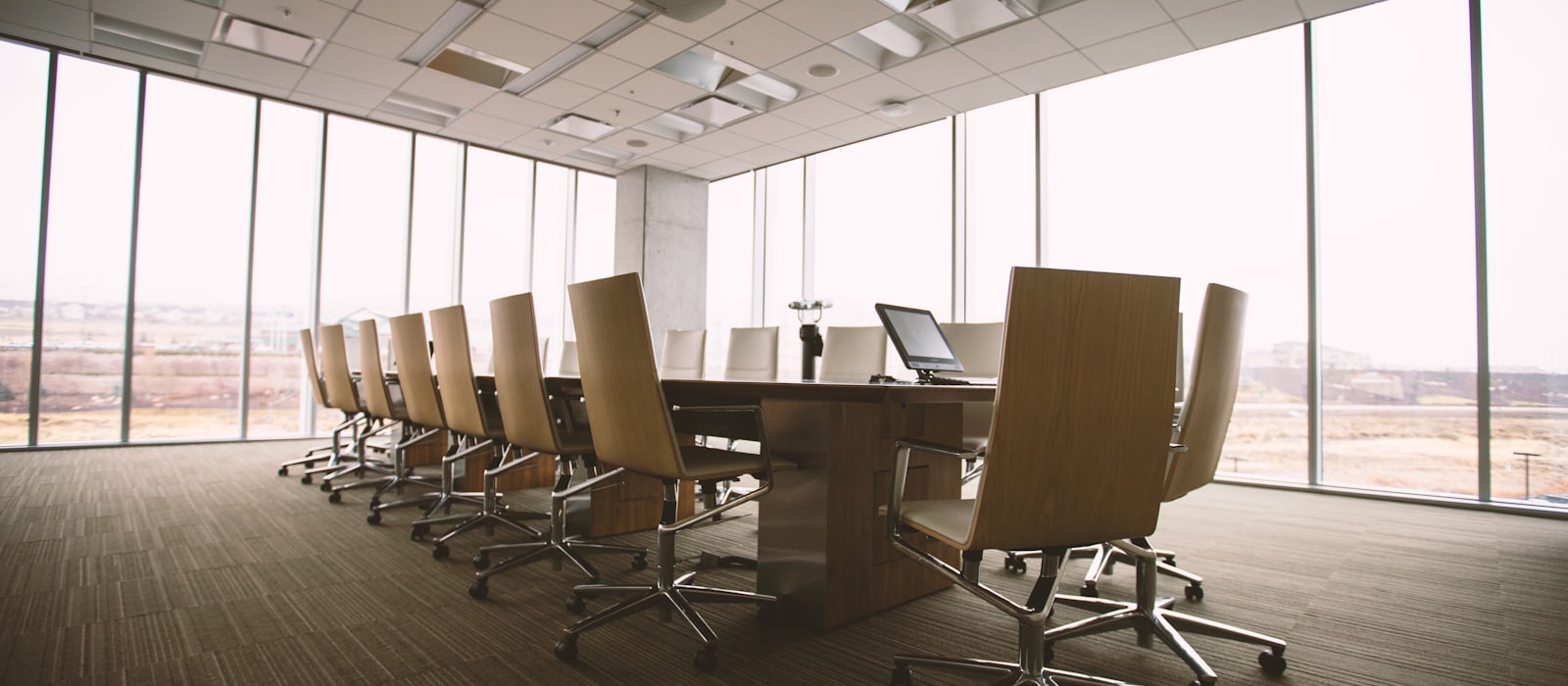 An empty boardroom with a long table and rows of chairs beside floor-to-ceiling windows