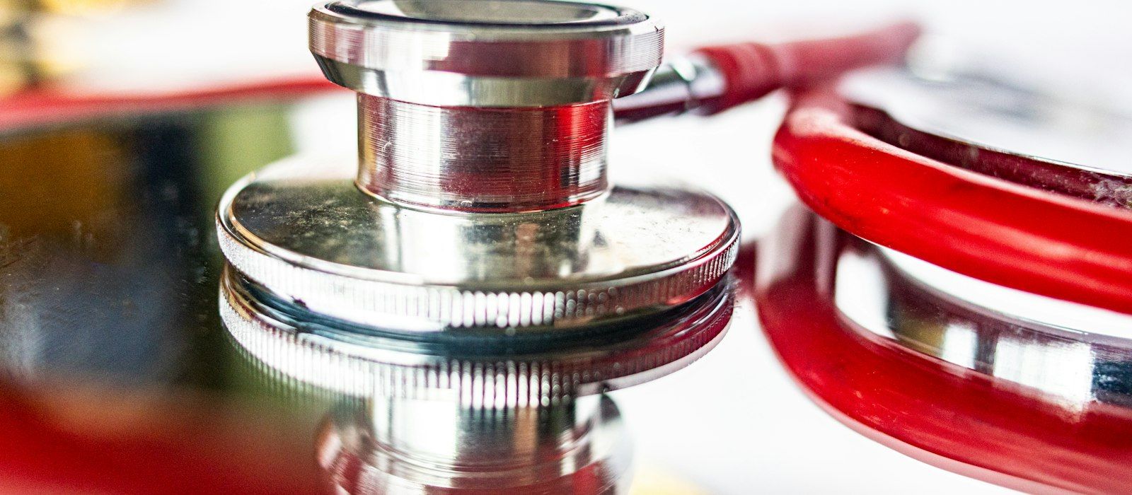 Close-up of a stethoscope chest piece with red tubing on a reflective surface