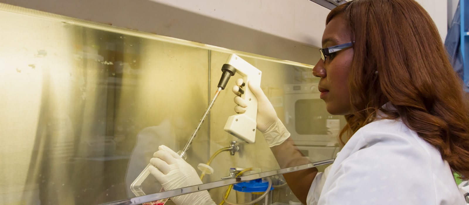A researcher in a lab coat using a pipette at a fume hood