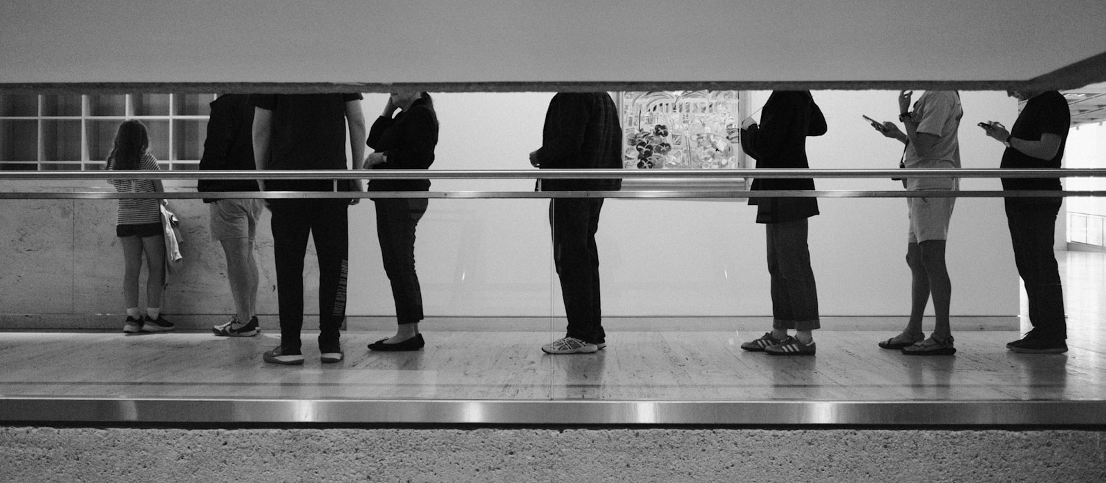 People standing in a line along a railing inside a large hall