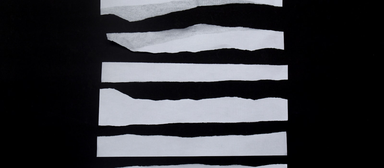 Torn strips of white paper laid out on a black surface
