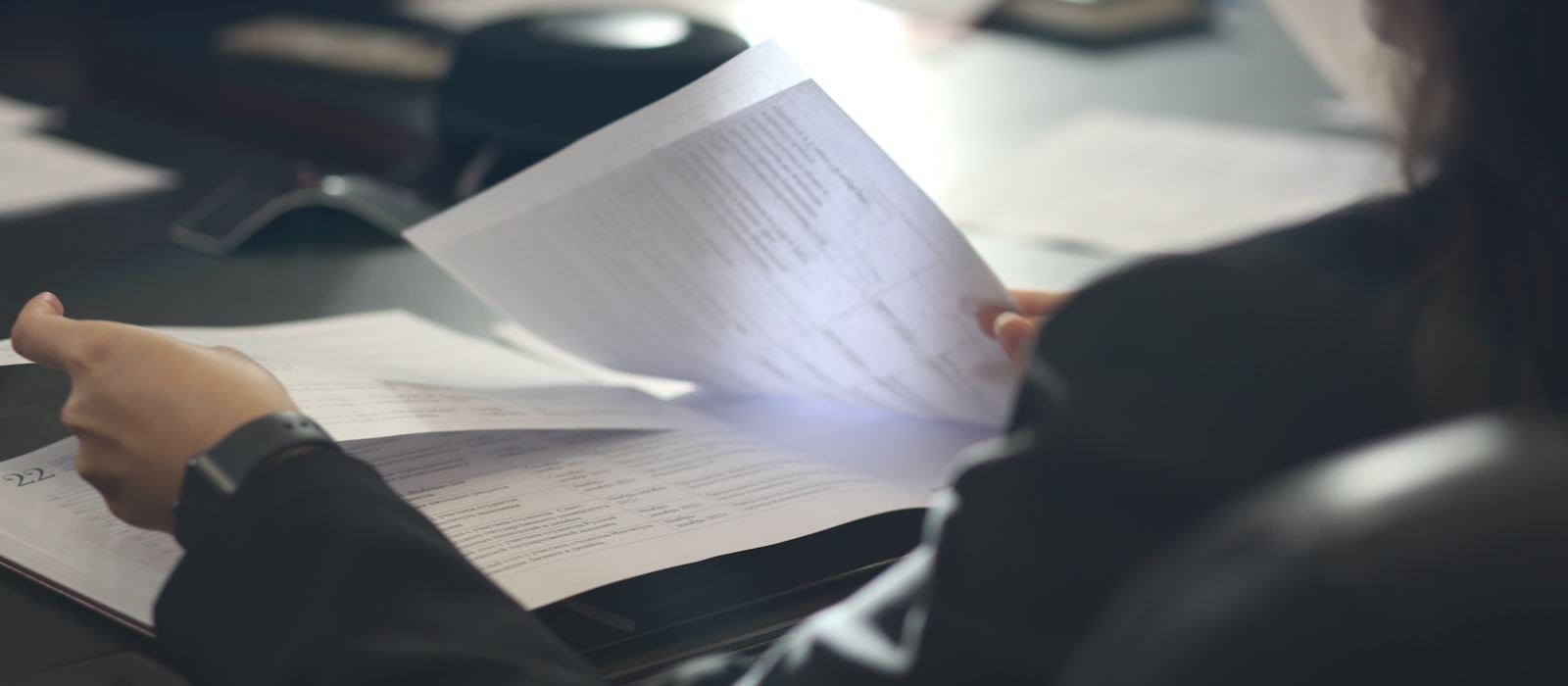 A person at a desk turning through the pages of a printed document