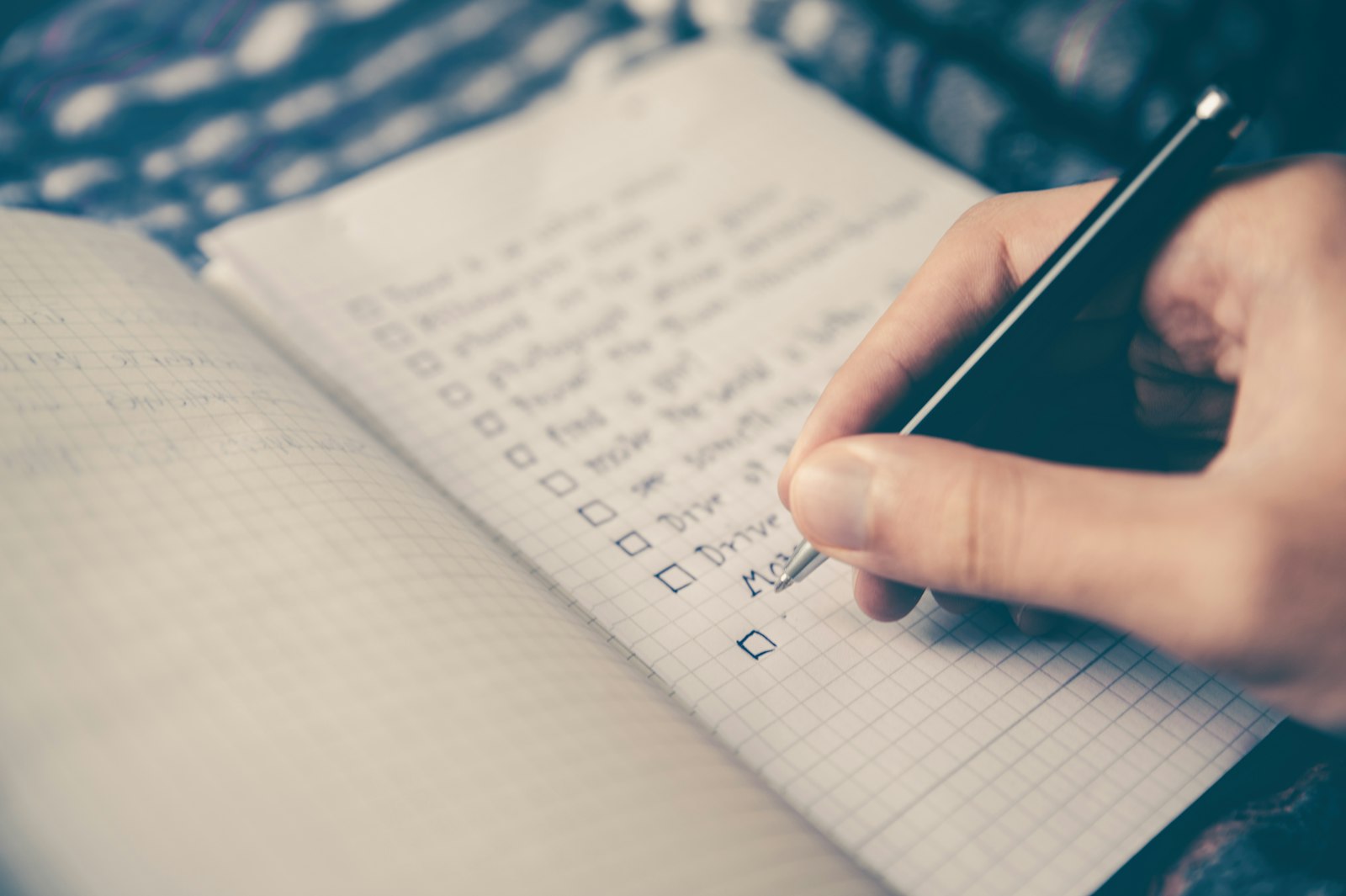 A hand writing a checklist in a grid-paper notebook