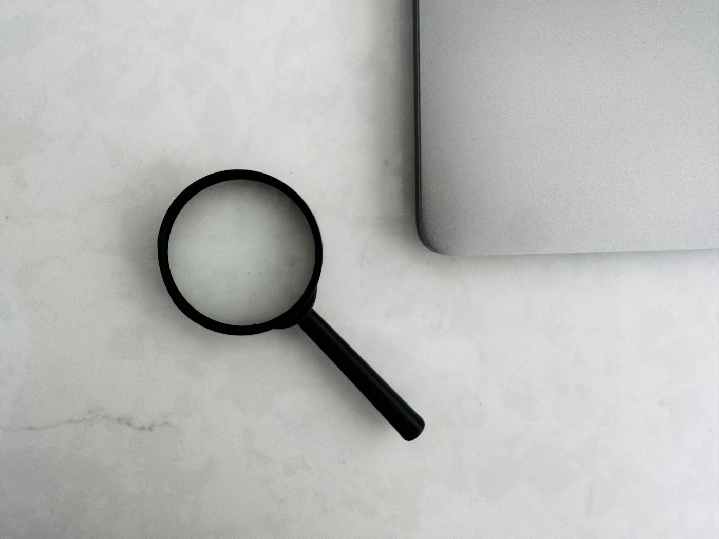 A magnifying glass beside a closed laptop on a plain surface