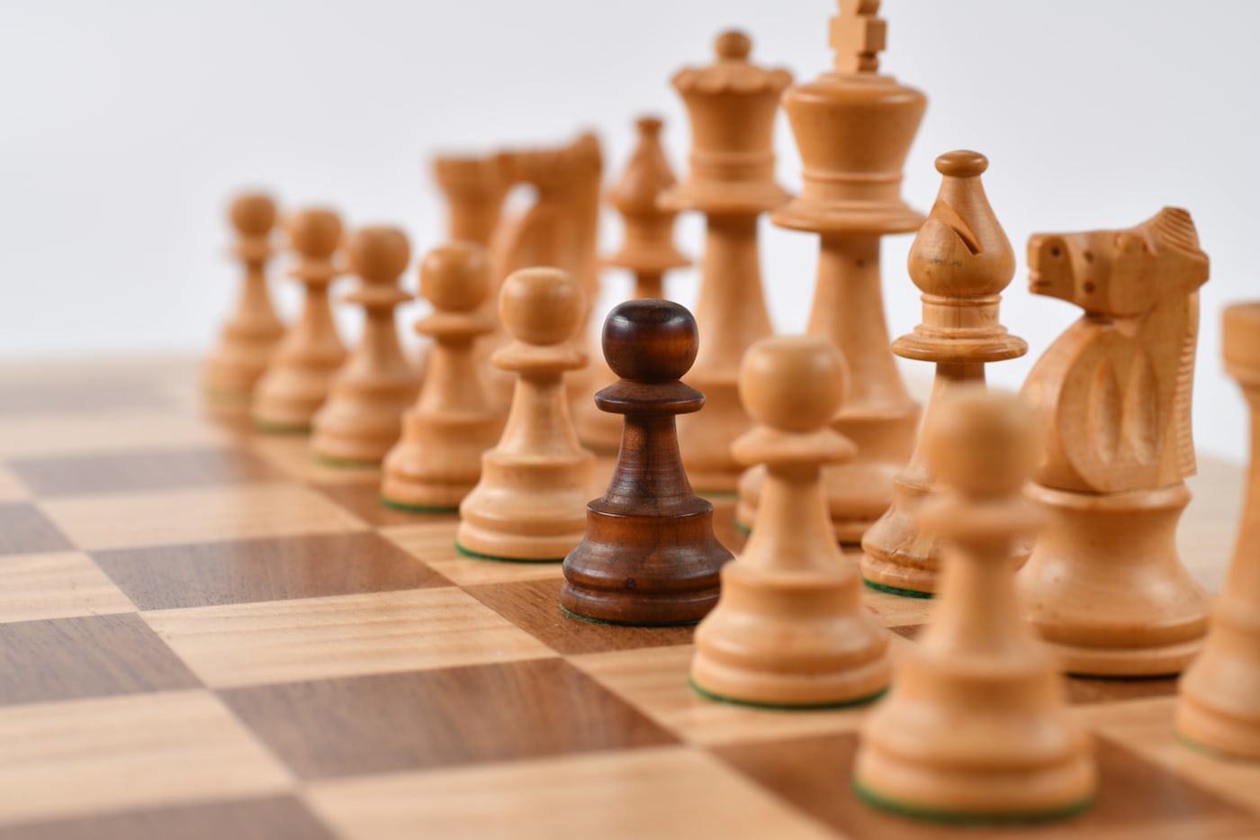 Chess pieces on a board with one dark pawn advanced among the white pieces