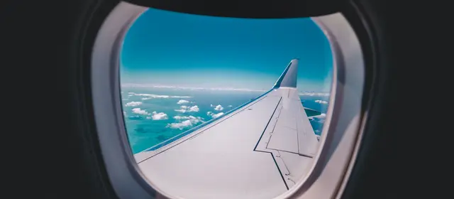 An aircraft wing seen through a cabin window above the clouds