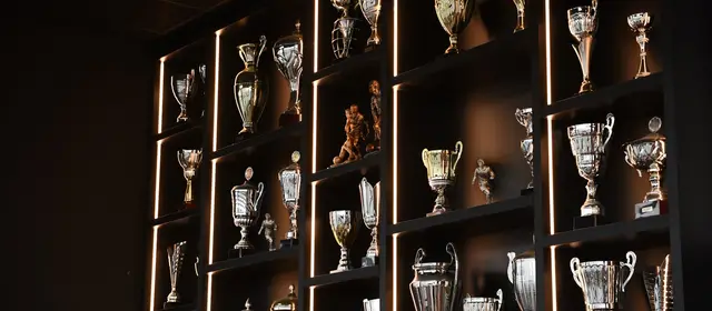 Shelves of silver and gold trophies lit from behind in a dark room