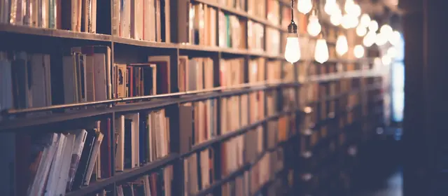 A long library aisle of packed bookshelves lit by hanging bulbs
