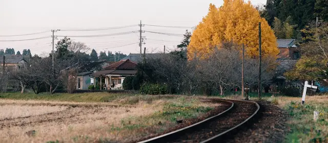 A single railway track curving past a rural station in autumn