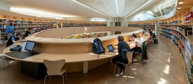 Students working at long curved desks in a bright university library