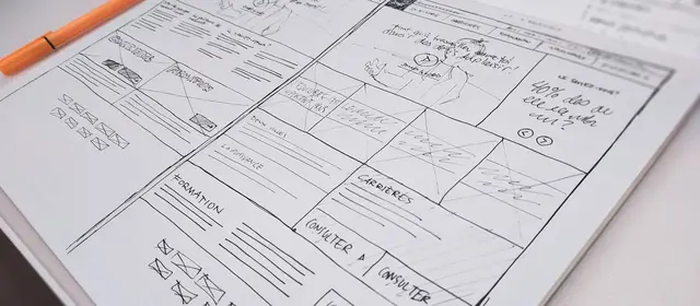 Hand-drawn interface wireframes on paper beside a marker pen