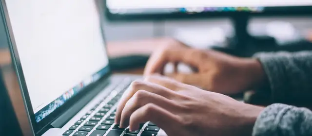 Hands typing on a laptop keyboard with a blank document on screen