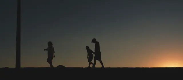 Silhouettes of an adult and children walking together at sunset