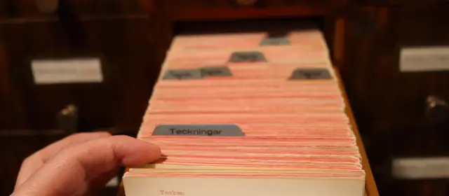 A hand lifting cards from a library catalogue drawer with labelled dividers