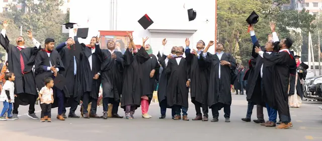 Graduates in black gowns throwing their caps in the air outdoors