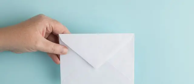 A hand holding a plain white envelope against a pale blue background
