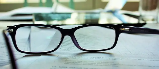 A pair of reading glasses resting on printed documents on a desk