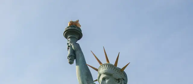 The torch and crown of the Statue of Liberty against a clear blue sky