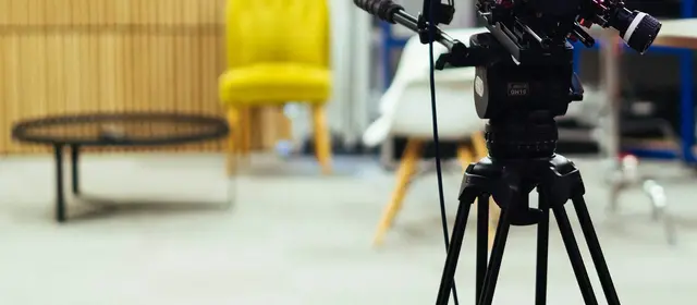 A video camera on a tripod in a studio with a yellow armchair behind it