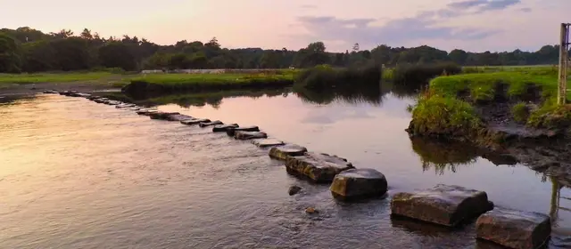 A line of stepping stones crossing a wide river at dusk