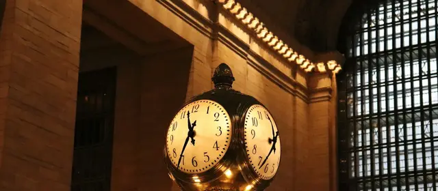 A brass four-faced clock in a grand train station concourse