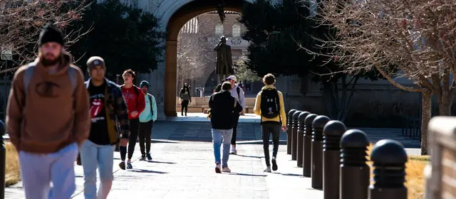 Students walking along a campus path toward a stone archway