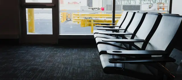 An empty row of seats at an airport departure gate, with the apron beyond the window