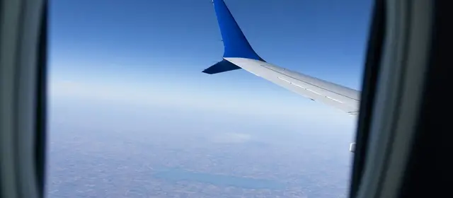 An airplane wing seen through a cabin window high above the clouds