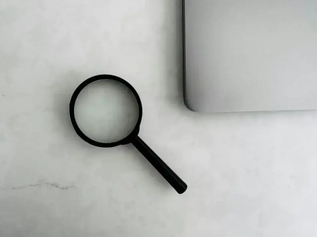 A magnifying glass beside a closed laptop on a plain surface