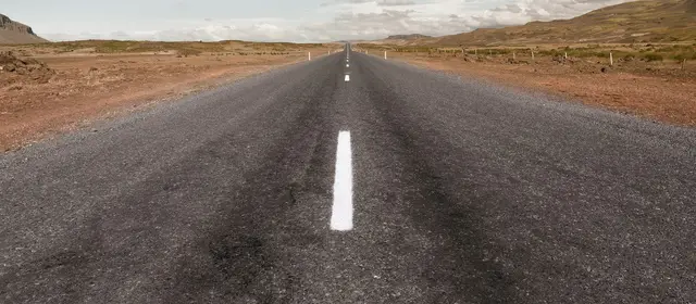A straight two-lane road running across open country toward low hills