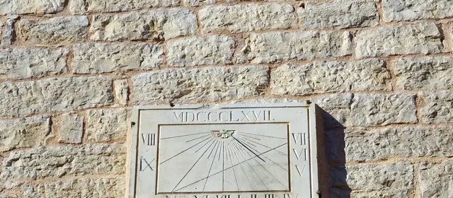 An old stone sundial with Roman numerals set into a sunlit stone wall
