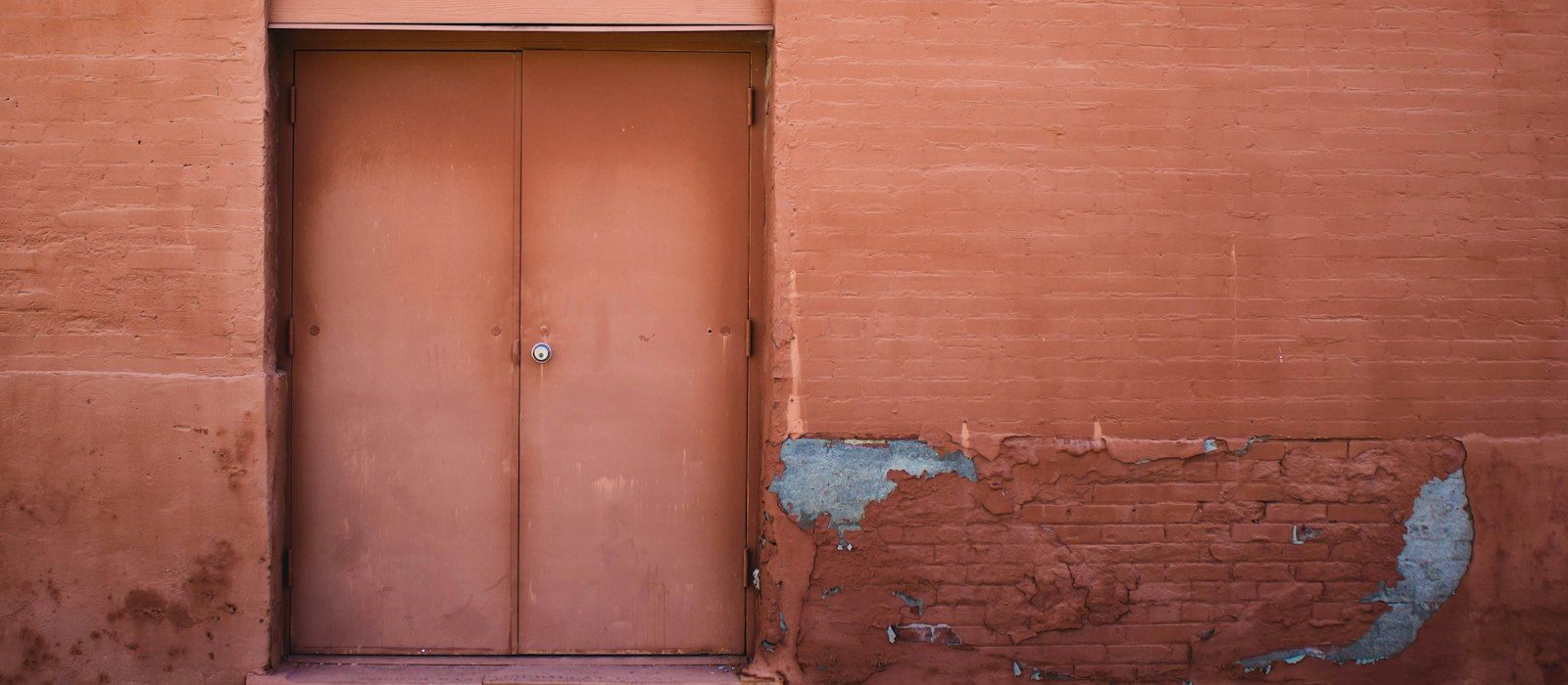 A closed pair of metal doors set in a weathered terracotta wall